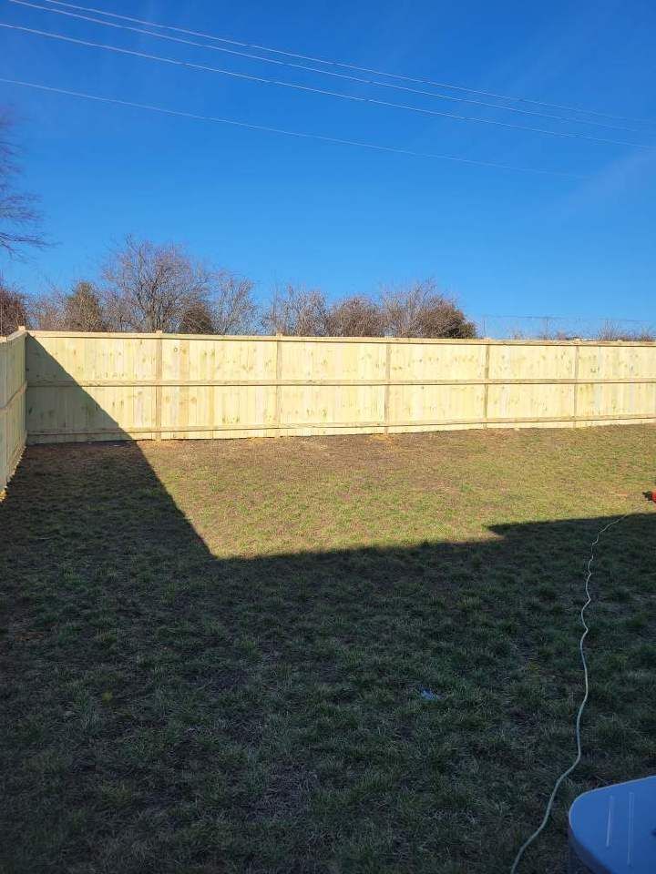 A backyard with a wooden fence and a blue sky in the background.