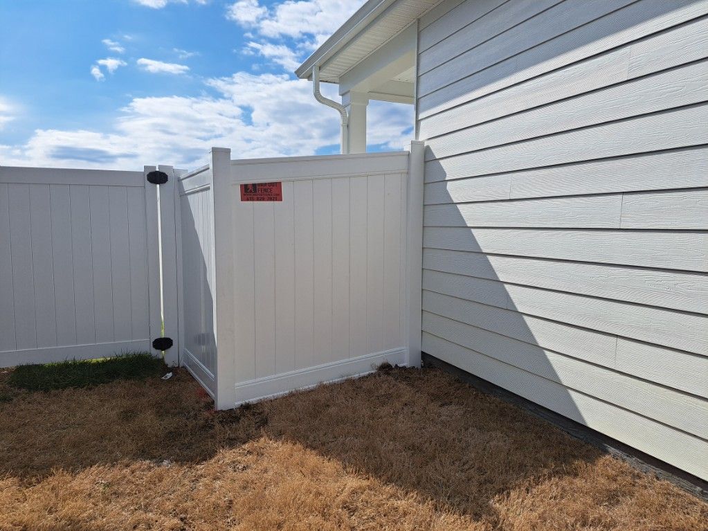 A white fence is sitting next to a white house.