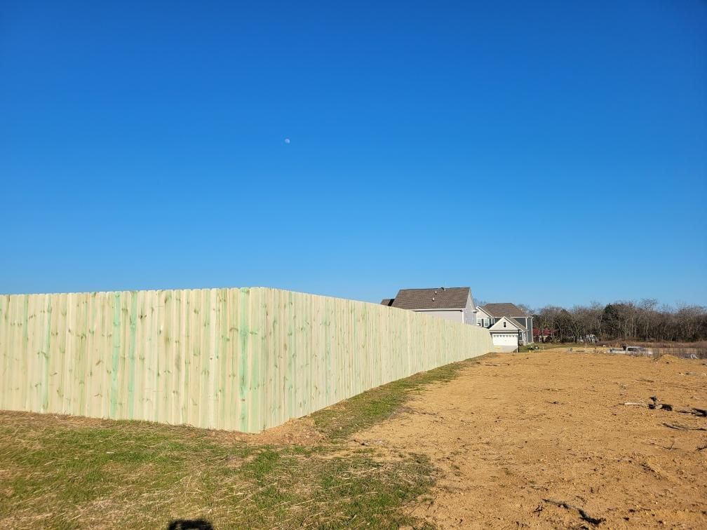 A wooden fence surrounds a dirt field with a house in the background.