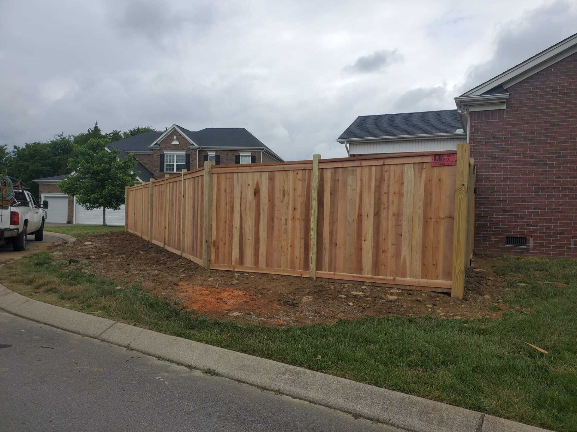 A wooden fence is being built in front of a brick house.