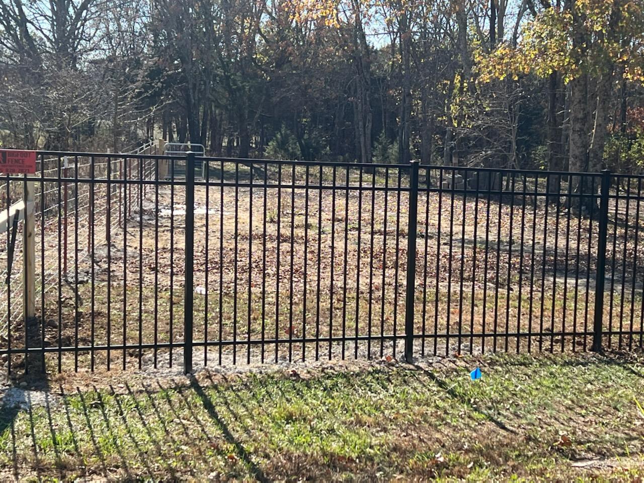 A black metal fence surrounds a grassy field with trees in the background.