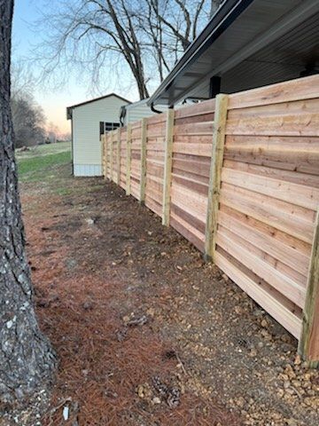 A wooden fence is sitting next to a tree in front of a house.