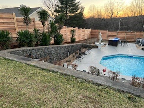 A large swimming pool is surrounded by a wooden fence and a stone wall.