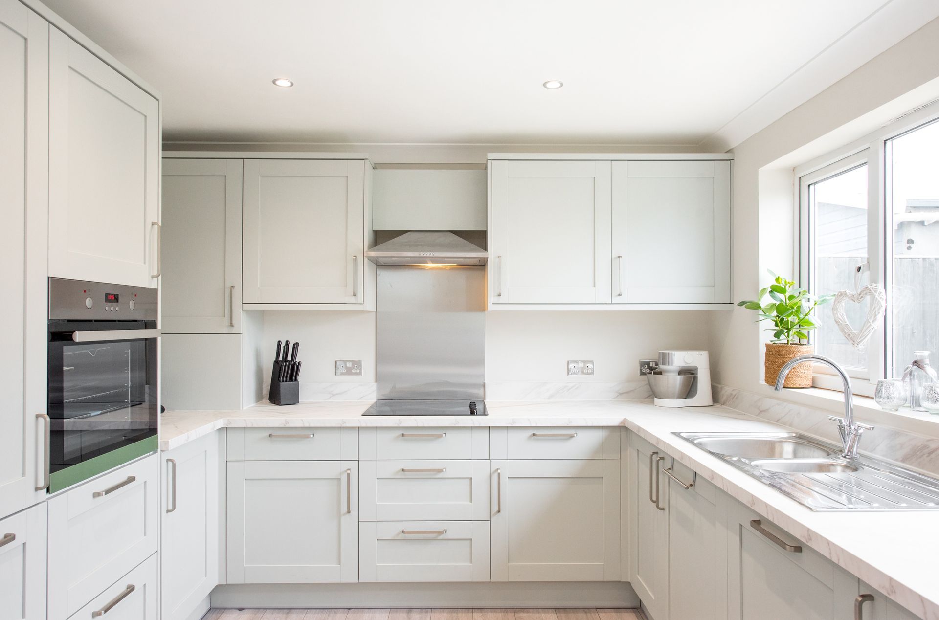A kitchen with white cabinets , a sink , a stove , and a window.