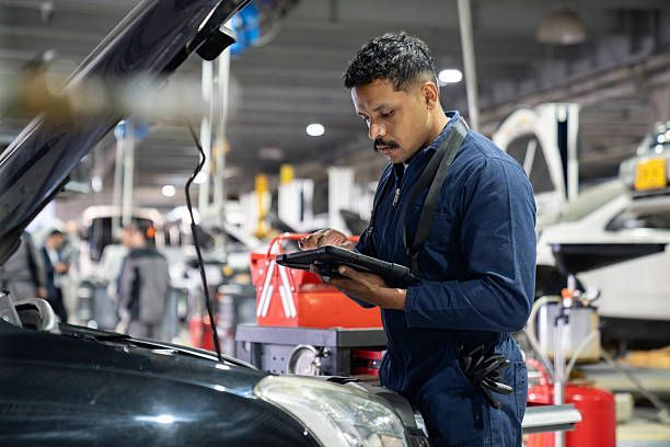Mechanic inspecting a car engine with a diagnostic tablet in an auto repair shop