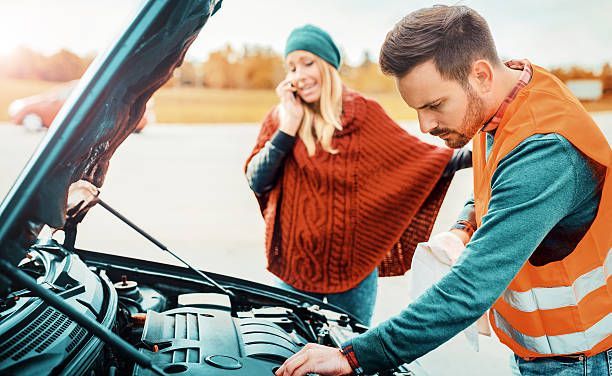 Two people inspecting a car engine, with the hood open and one wearing a high-visibility vest.