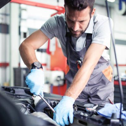 Mechanic in gray overalls and blue gloves working under a car hood in a garage
