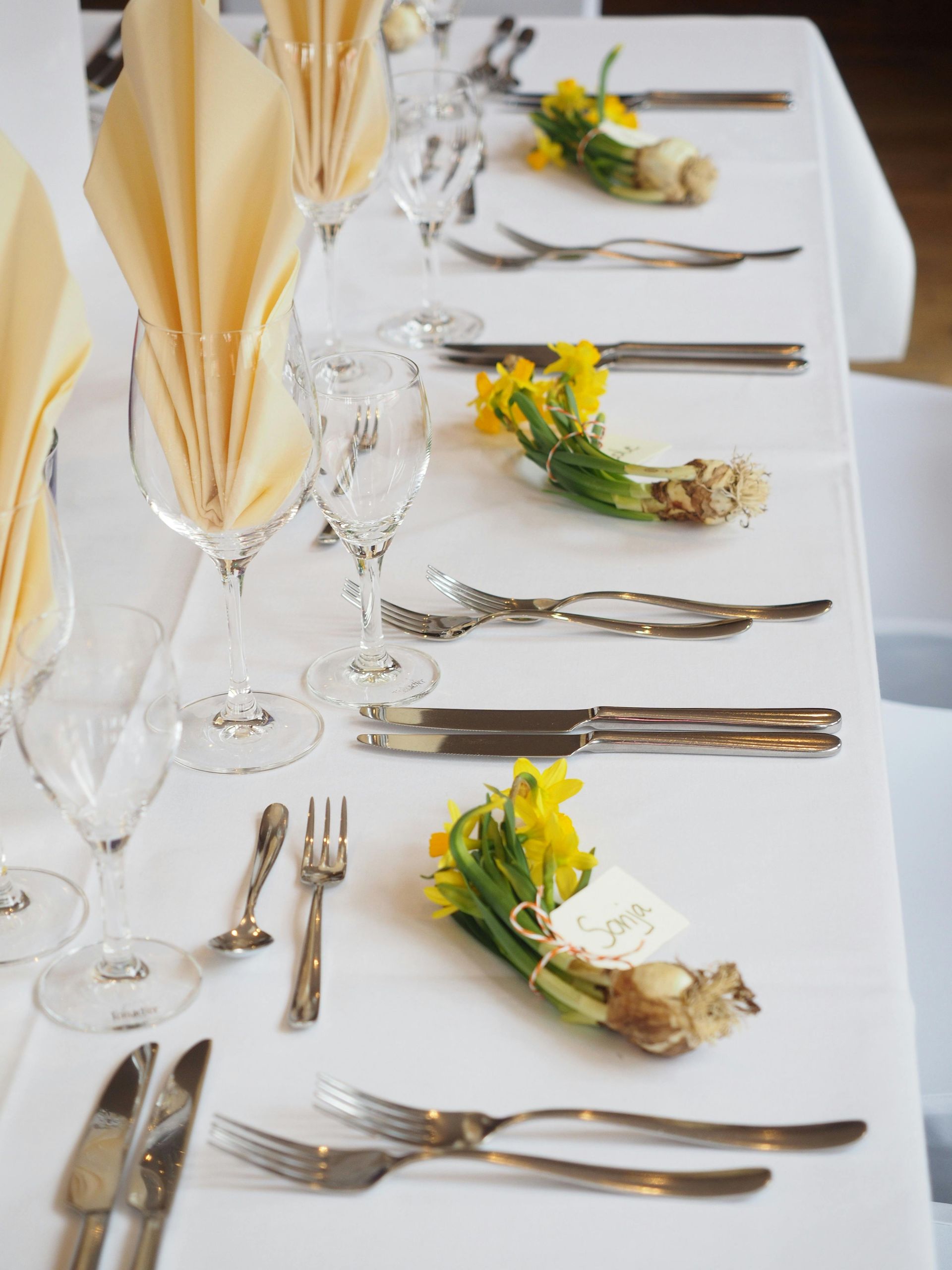 Formal table setting with napkins, glasses, and flower bundles.