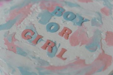 Gender reveal cake with pink and blue frosting and fondant letters that spell 