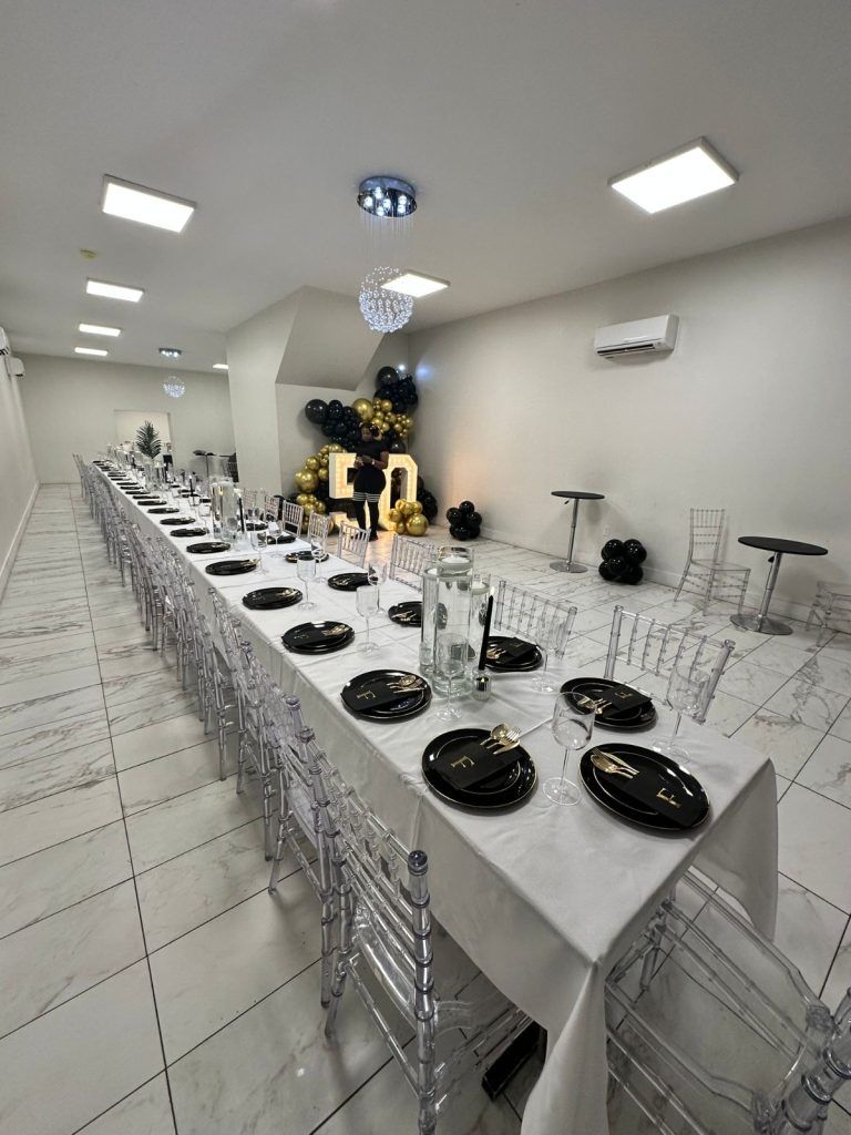 Long table set for a party in a white room, with black and gold decorations.