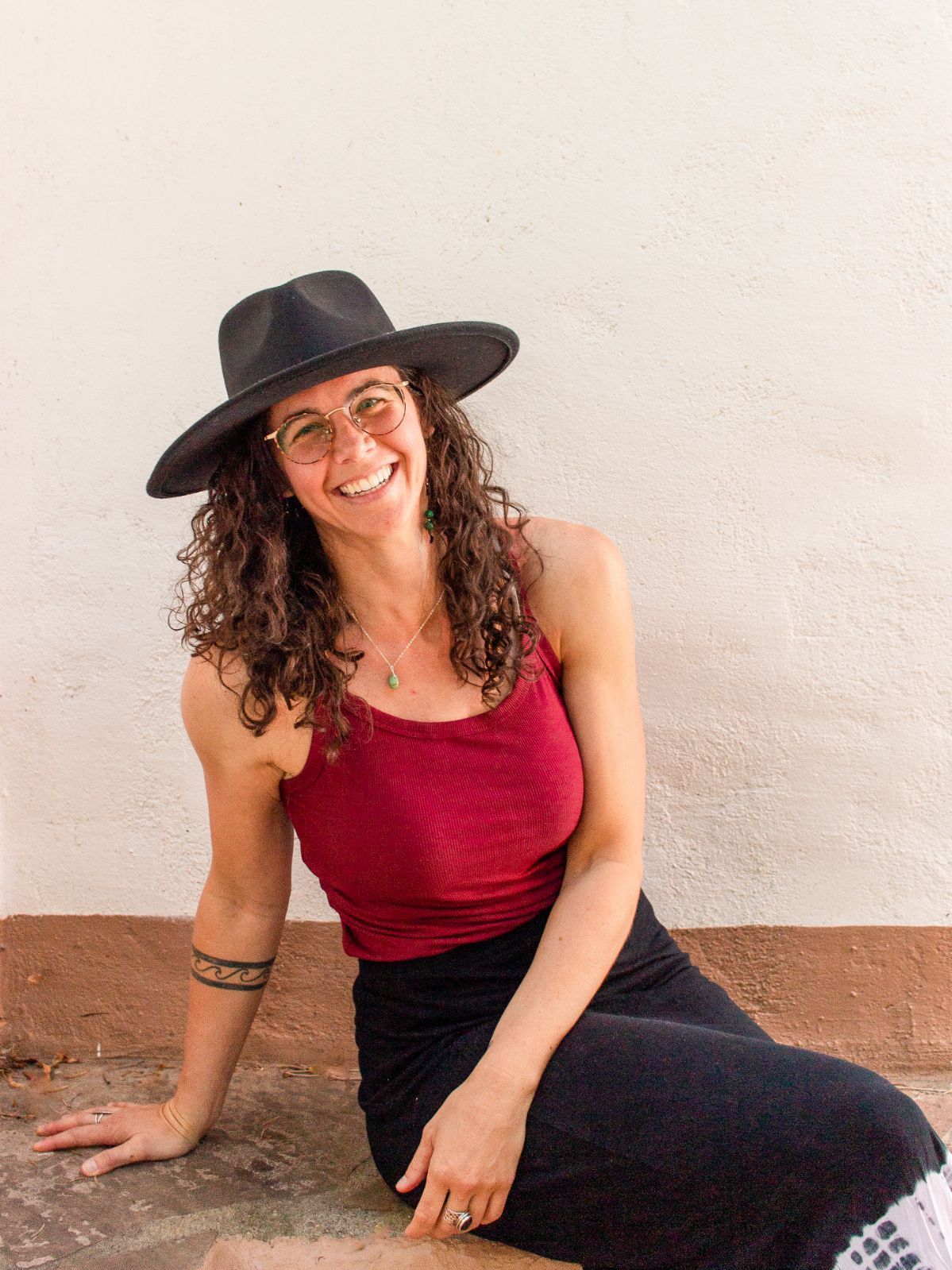 A woman wearing a hat and glasses is sitting on the ground.