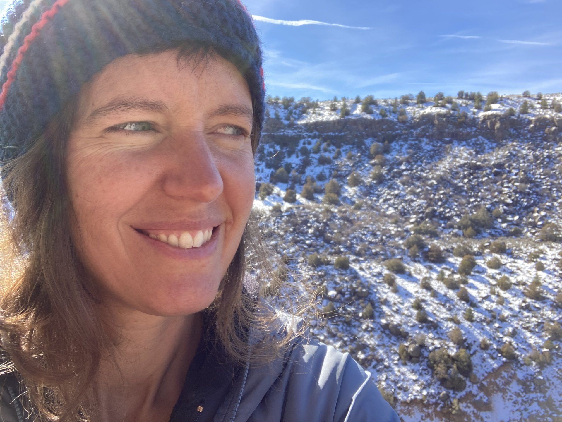 A woman wearing a hat is smiling in front of a snowy landscape.