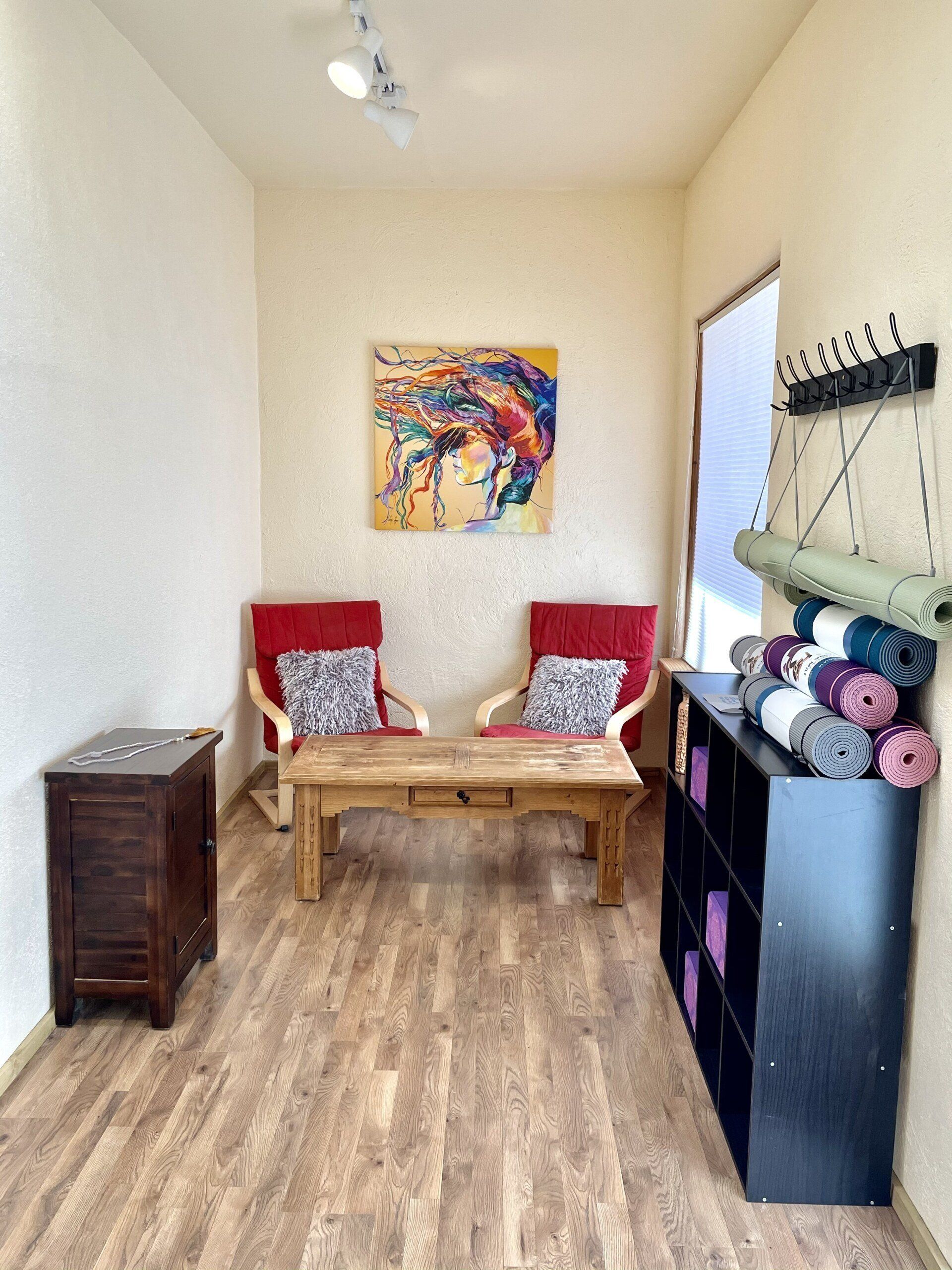 A living room with two chairs , a coffee table , and a painting on the wall.