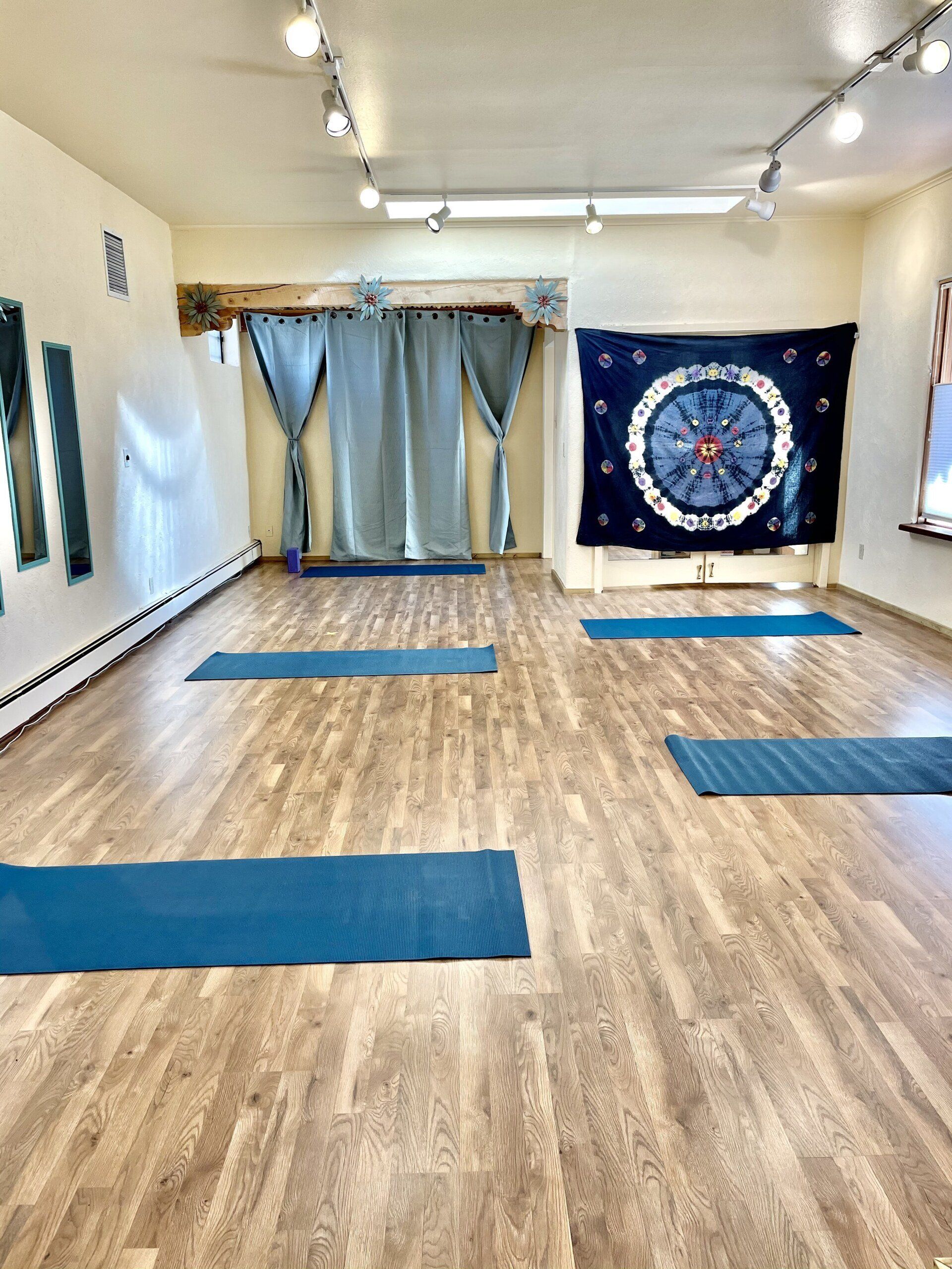 A large room with wooden floors and blue yoga mats.