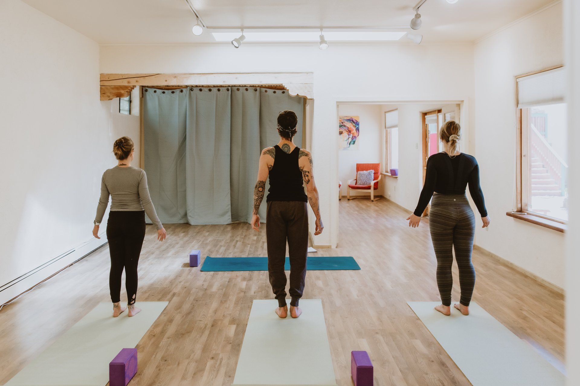 Three women are standing on yoga mats in a room.