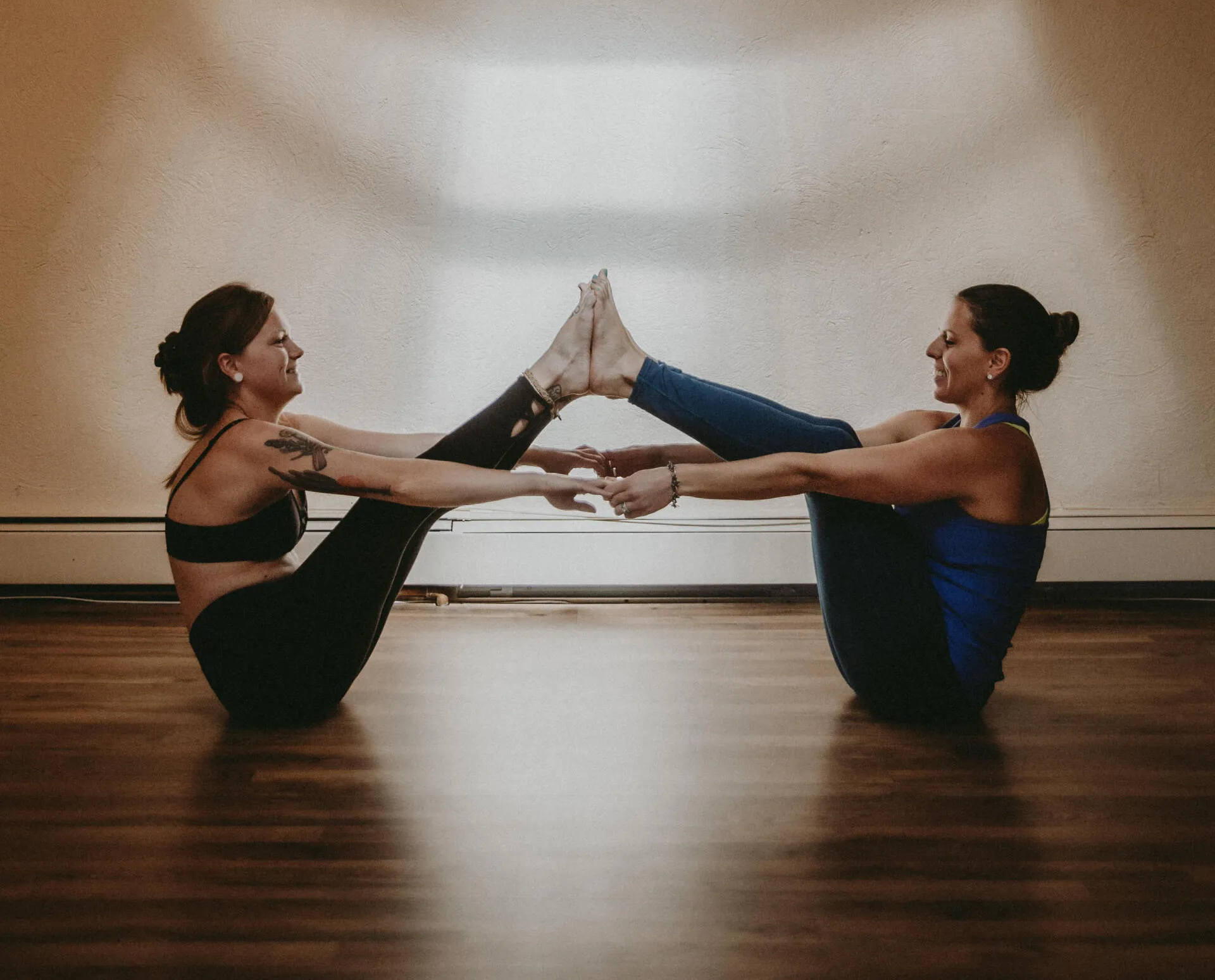 Two women are doing yoga together on a wooden floor.