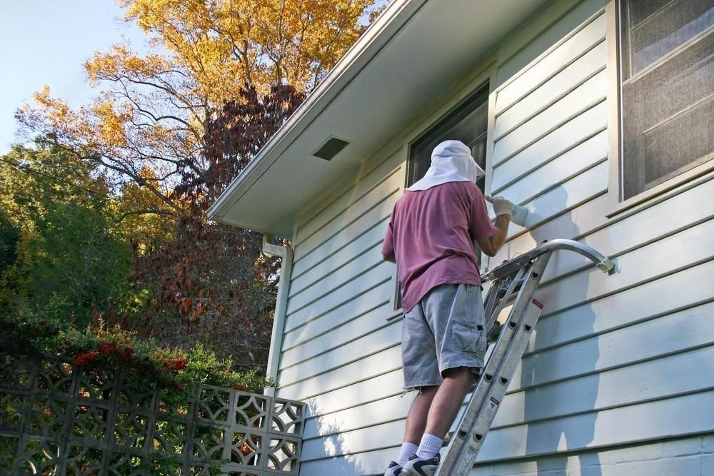 A man on a ladder paints the side of a house