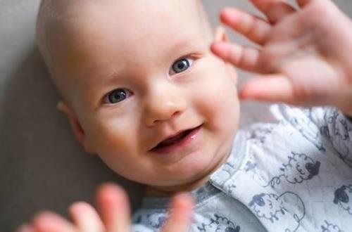 Smiling baby with hands raised, wearing a light blue onesie.