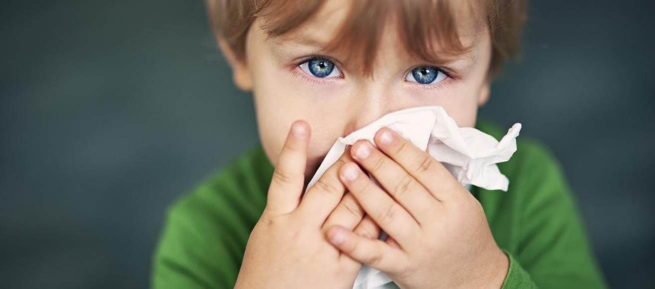 A person with blue eyes holding a white tissue to their nose, appearing unwell.