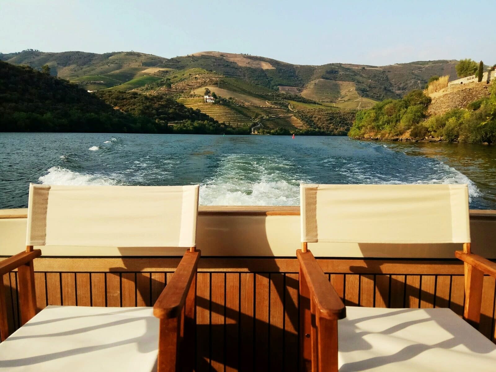 Duas cadeiras estão sobre um deck de madeira com vista para um lago.