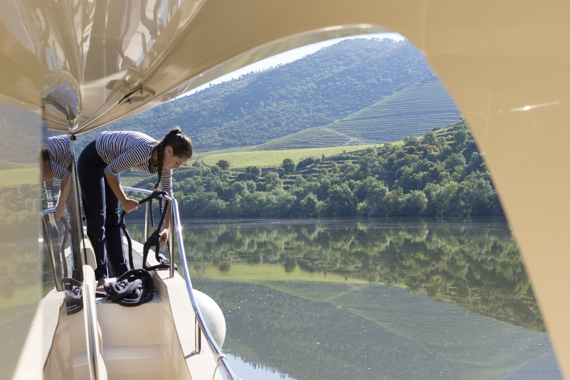A woman is standing on the side of a boat overlooking a lake.