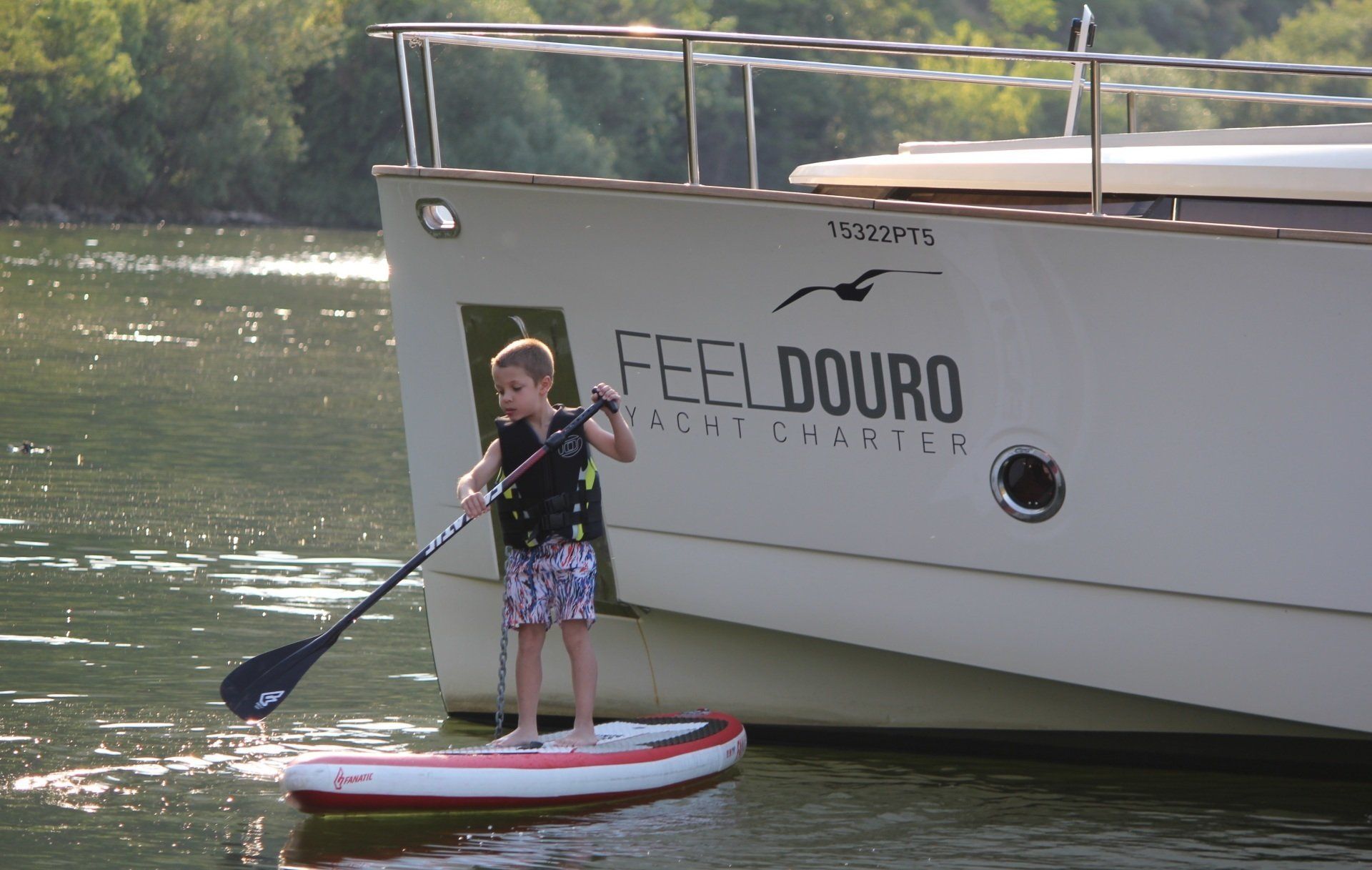 A boy on a paddle board in front of a boat that says feel douro