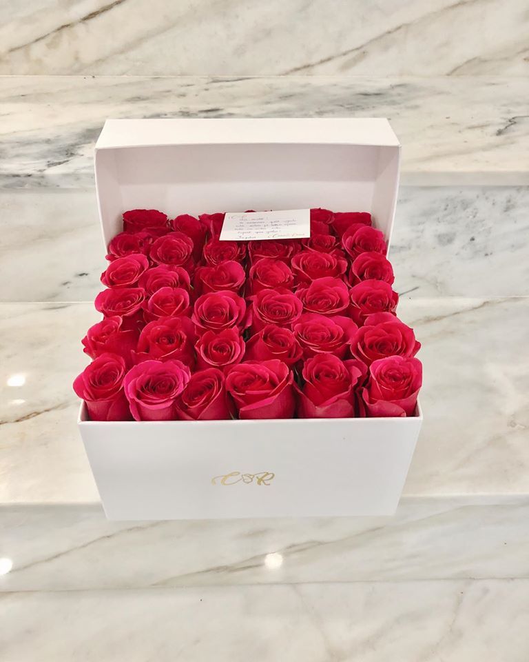 A white box filled with red roses is sitting on a marble counter.