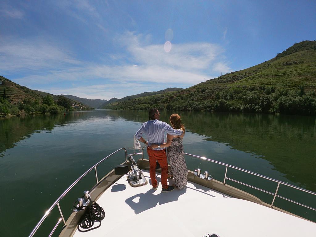 A man and a woman are standing on the back of a boat looking out over a lake.