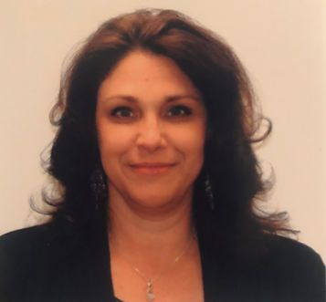 A woman wearing a black jacket and a necklace smiles for the camera