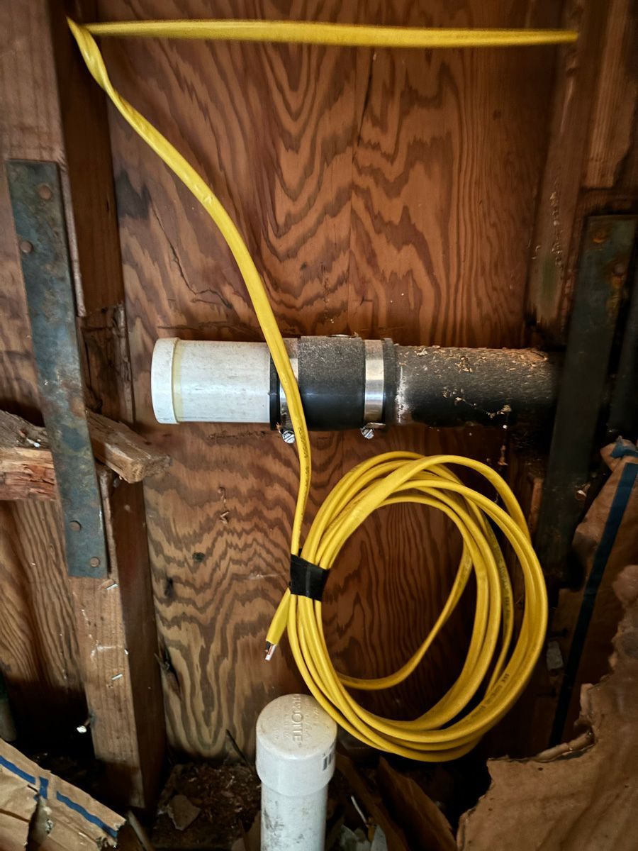 A yellow wire is connected to a pipe in a wooden room.