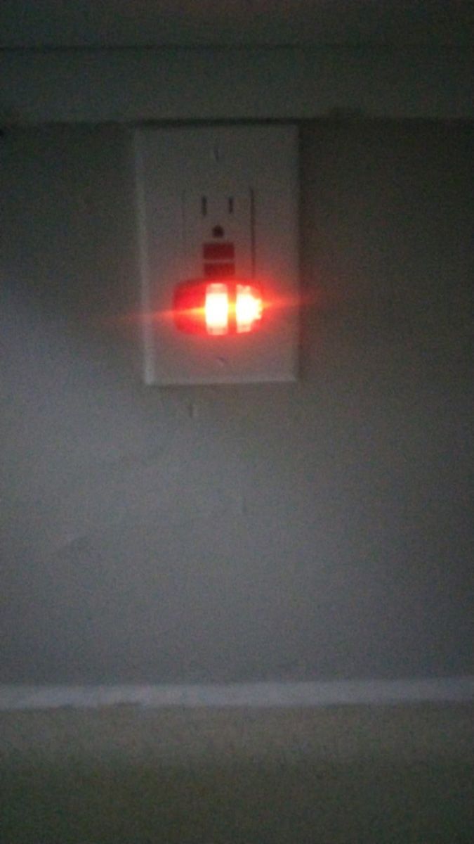 A red light is coming out of an electrical outlet on a wall.