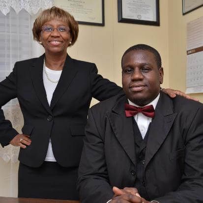 Woman in suit with hand on man's shoulder; both smiling in office setting.