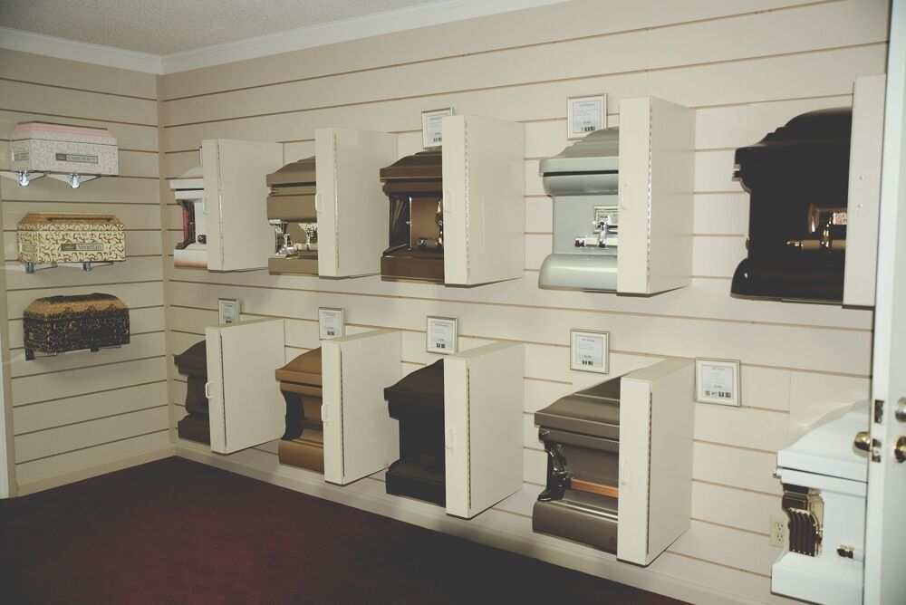 Coffins on display in a showroom, mounted on a striped wall, various colors and styles.