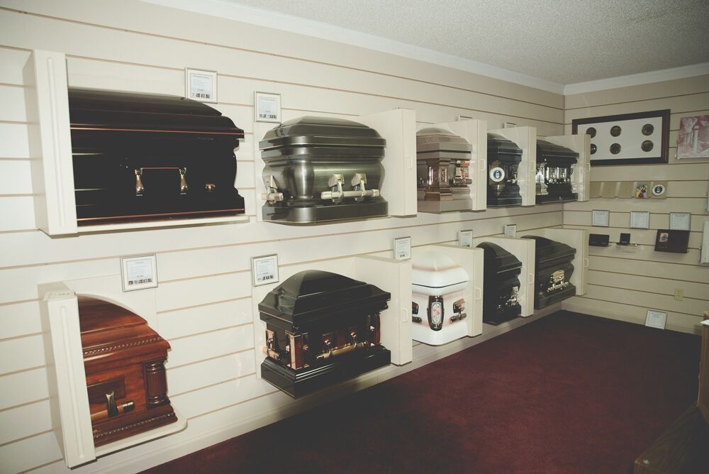 Caskets displayed on a wall in a funeral home showroom with price tags.