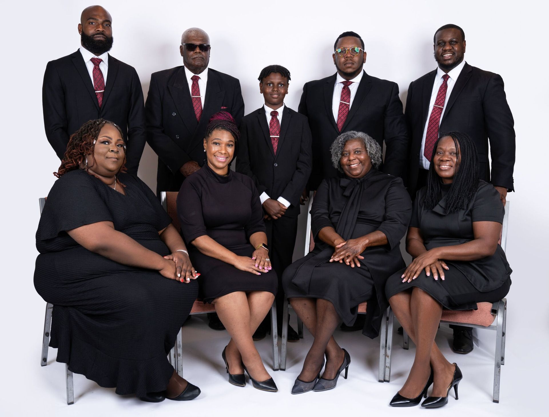 Group of people in formal attire, some seated, against a white backdrop.