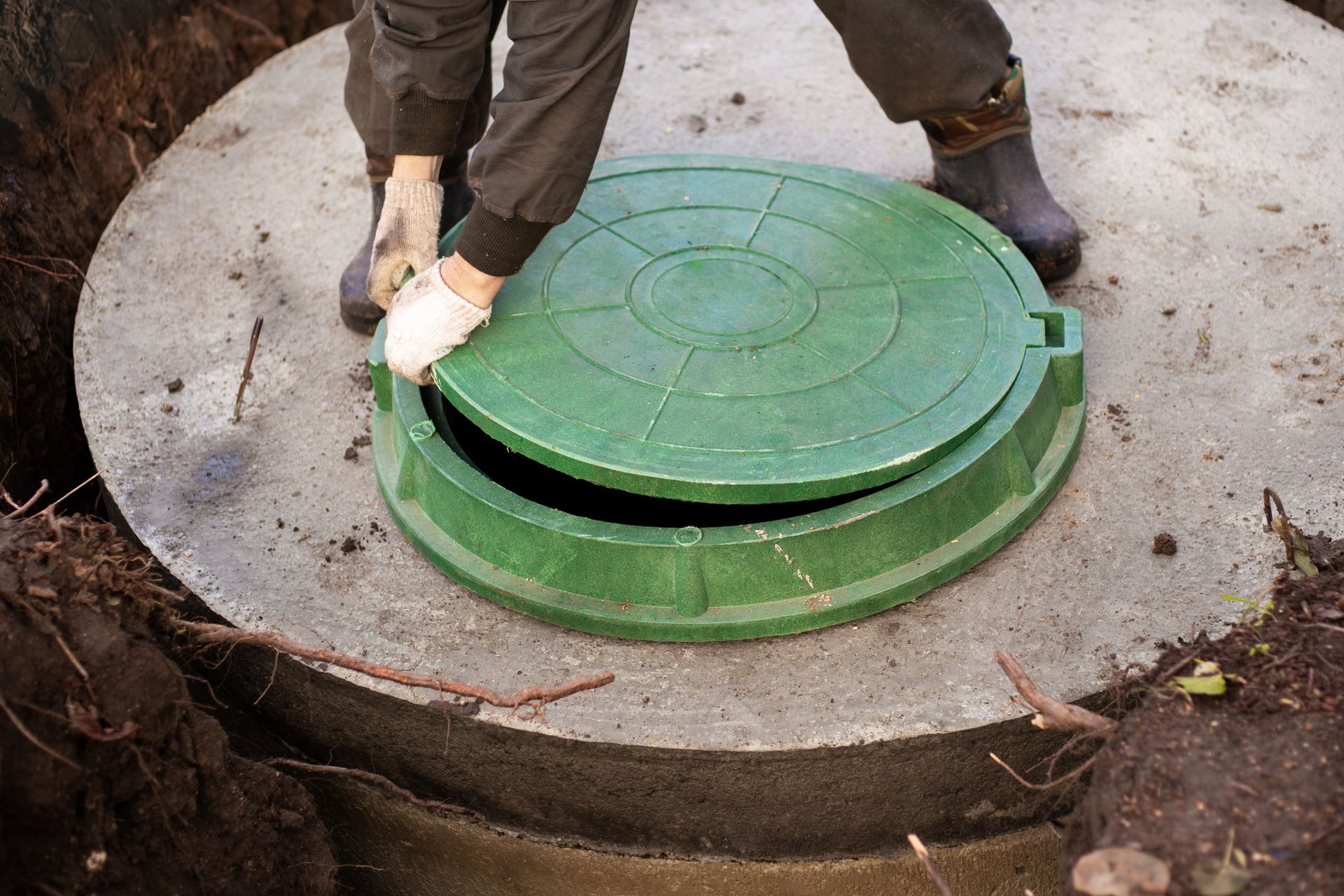 A man is opening a green manhole cover in a hole.