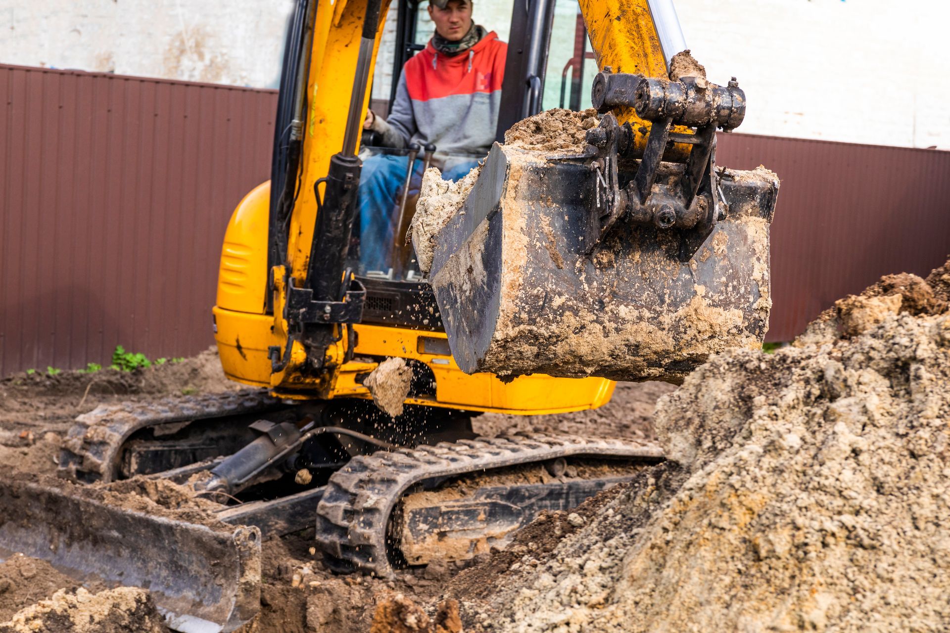 A man is driving a yellow excavator on a dirt road.