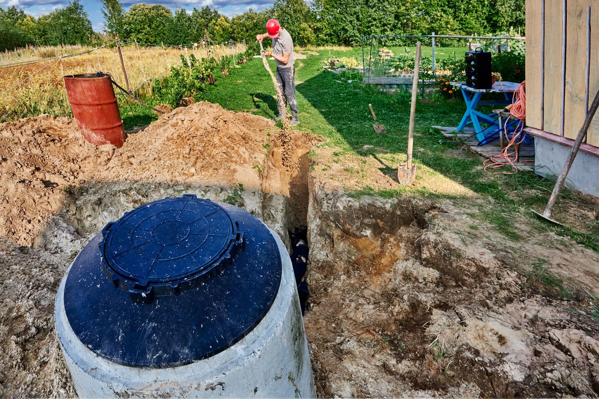 A man is digging a hole in the ground next to a septic tank.