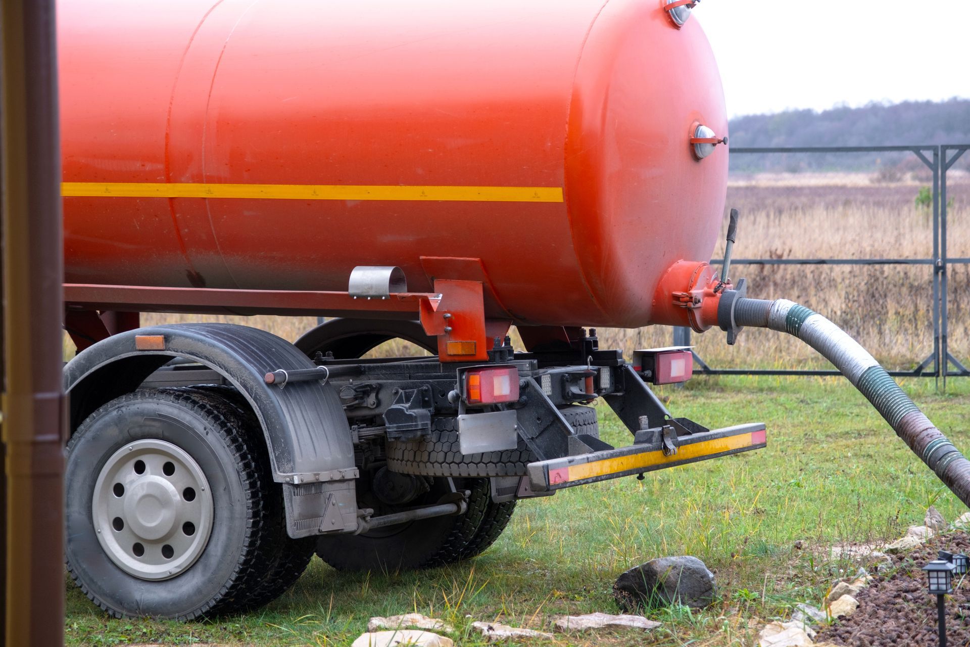 A red tanker truck is pumping water into a field.
