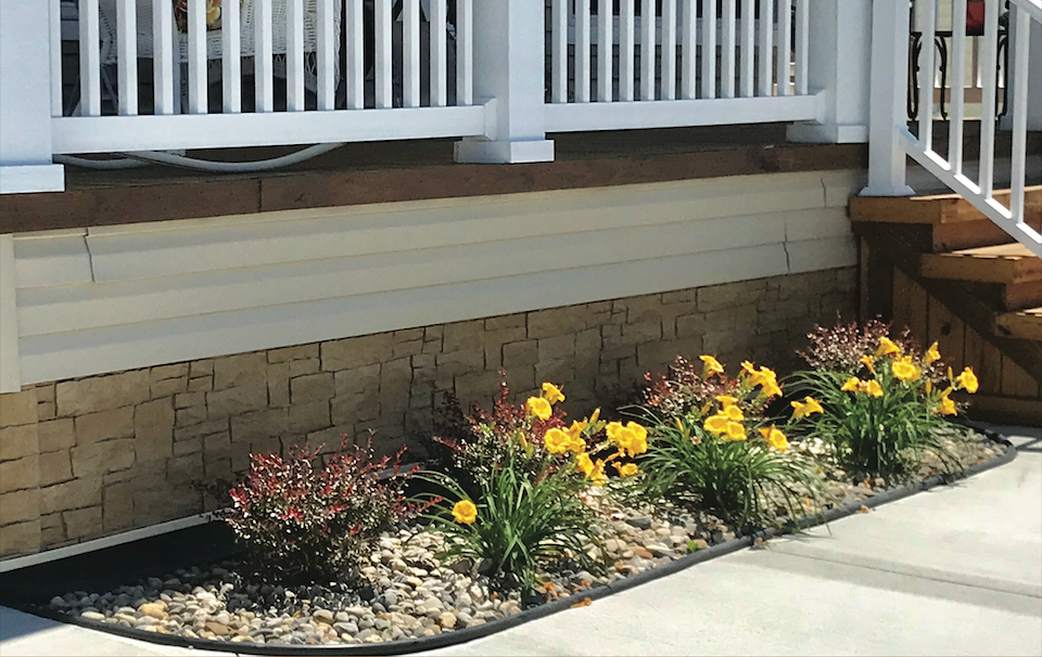 A garden with yellow flowers in front of a house with stairs.