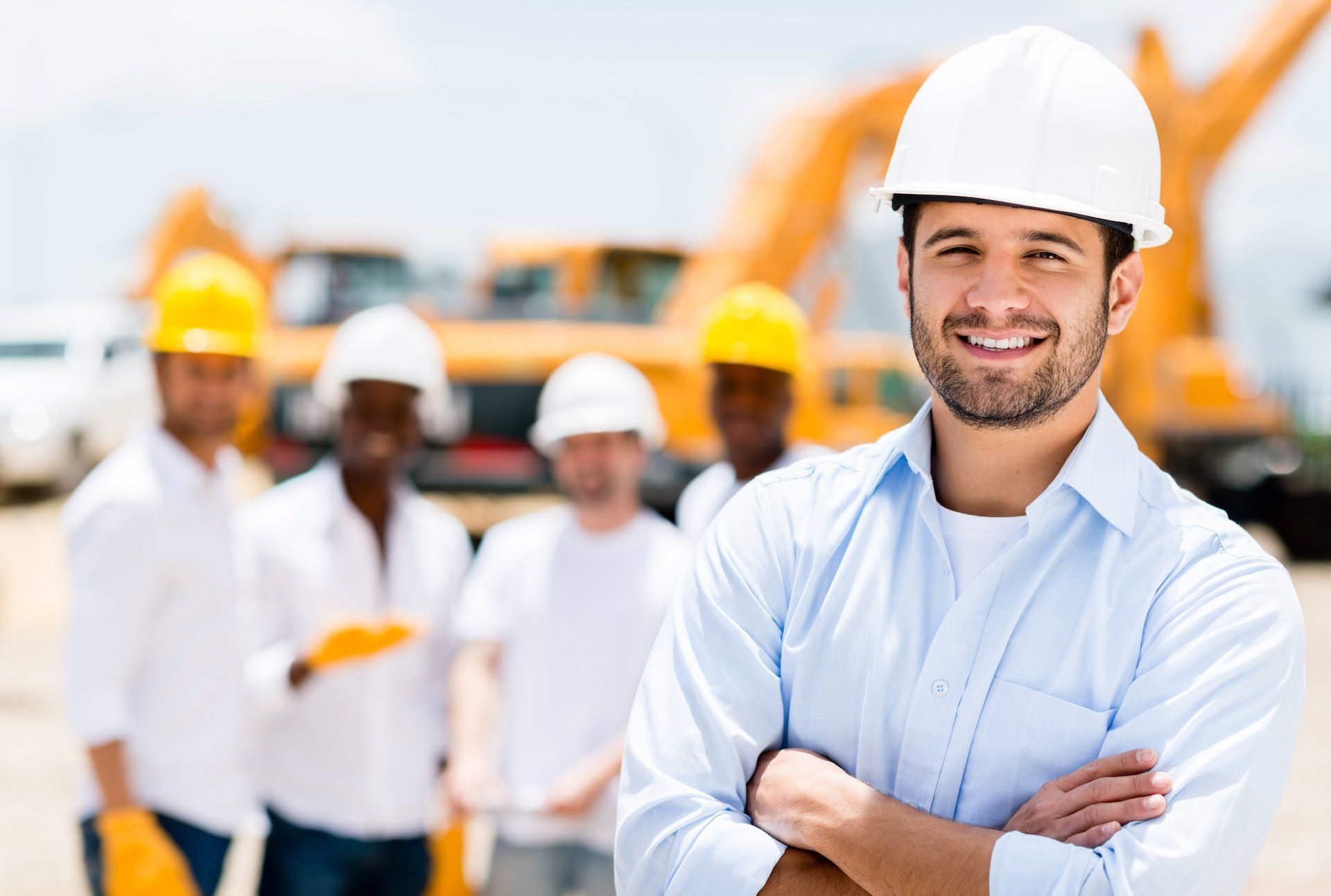 A man wearing a hard hat is standing in front of a group of construction workers.