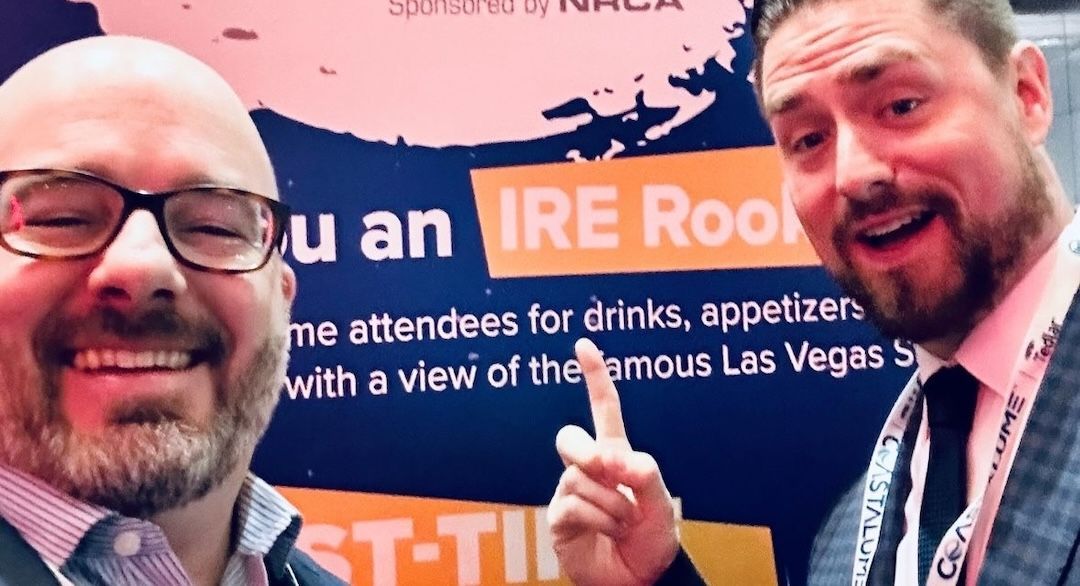 Two men are posing for a picture in front of a sign that says ire rook