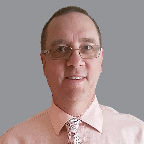 A man wearing glasses and a pink shirt and tie is smiling.