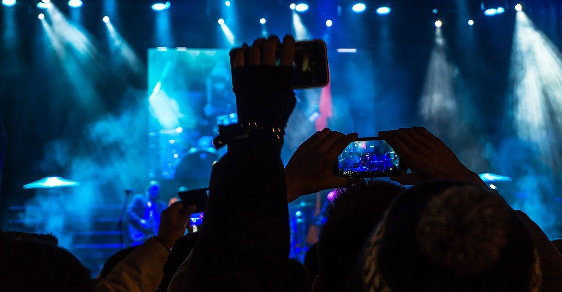 A crowd of people are taking pictures of a concert with their cell phones.