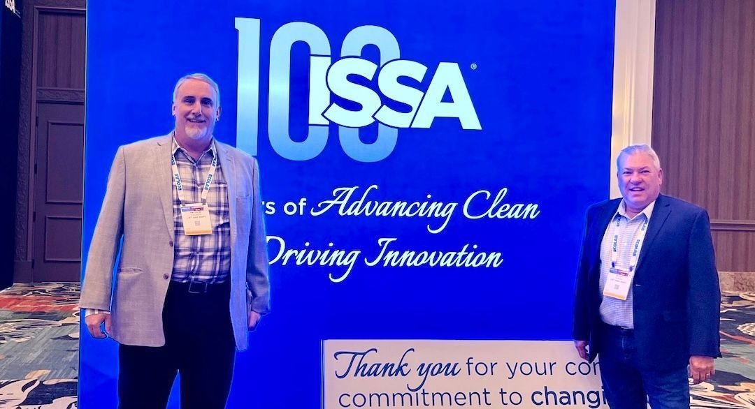 Two men are standing in front of a sign that says issa