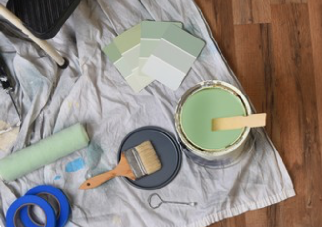 A bucket of green paint is sitting on a towel on a wooden floor.