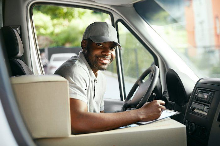 A delivery man is sitting in the driver 's seat of a van.
