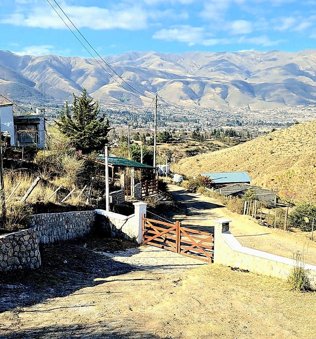 Un camino de tierra rústico que conduce a una puerta de madera, con un fondo de cadena montañosa y edificios.