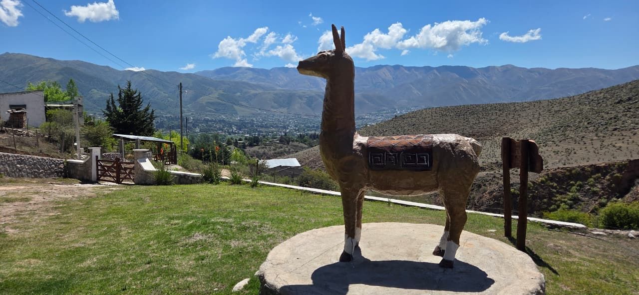 Una estatua de llama sobre una losa de hormigón, con montañas al fondo bajo un cielo azul.