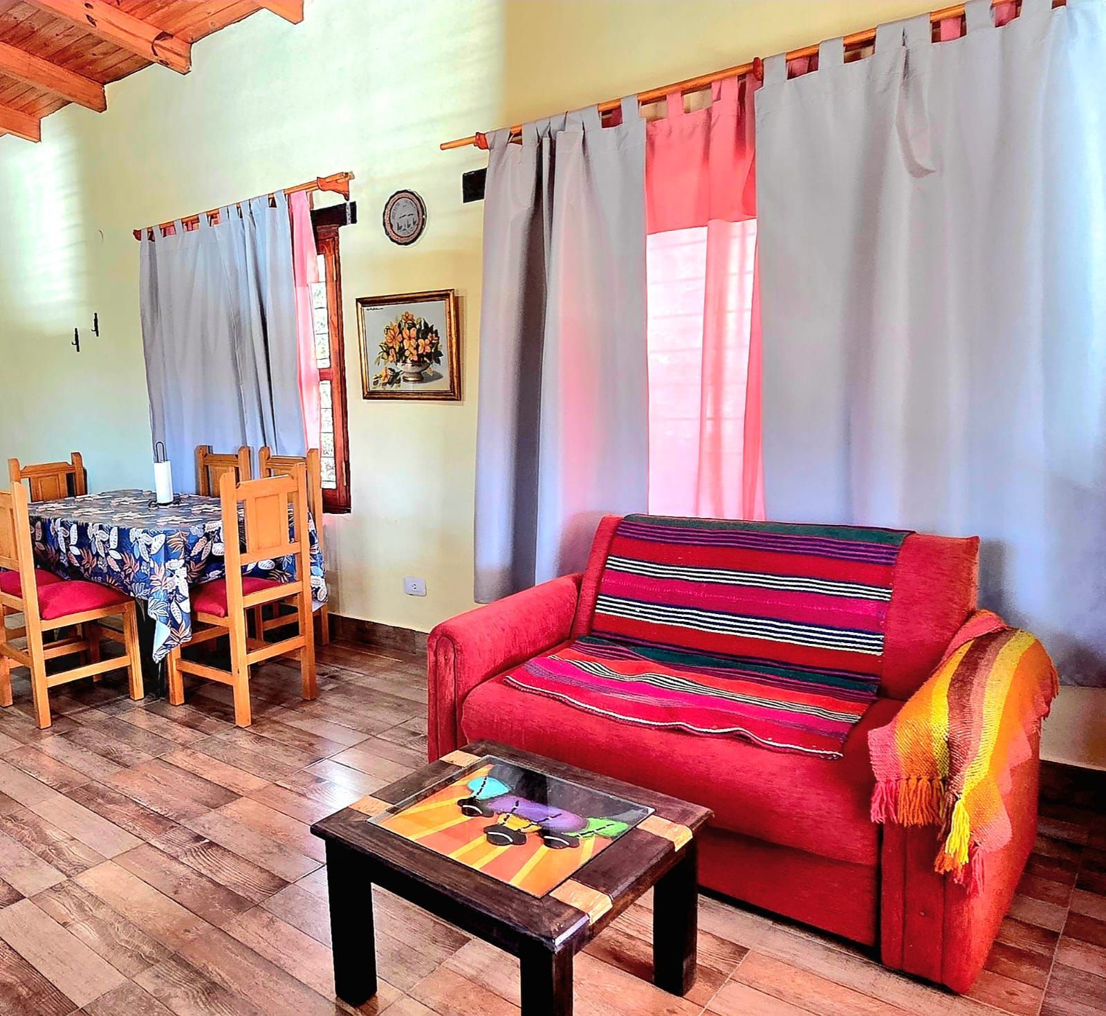 Acogedora sala de estar con sofá rojo, mesa de comedor, alfombra colorida, piso de madera y paredes amarillas.